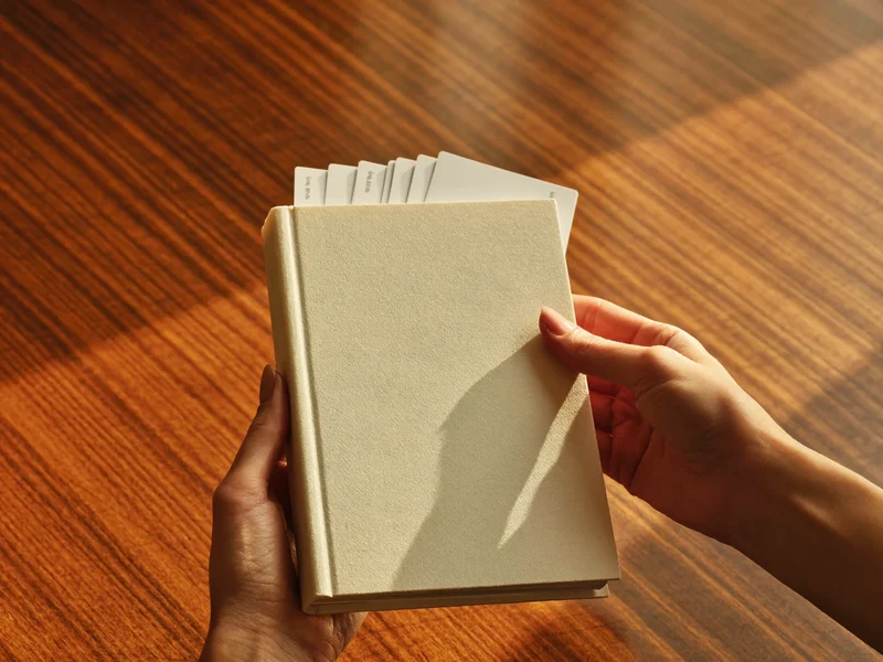 Hände einer Lehrperson mit Taschenbuch und Stapel unbeschrifteter Karteikarten